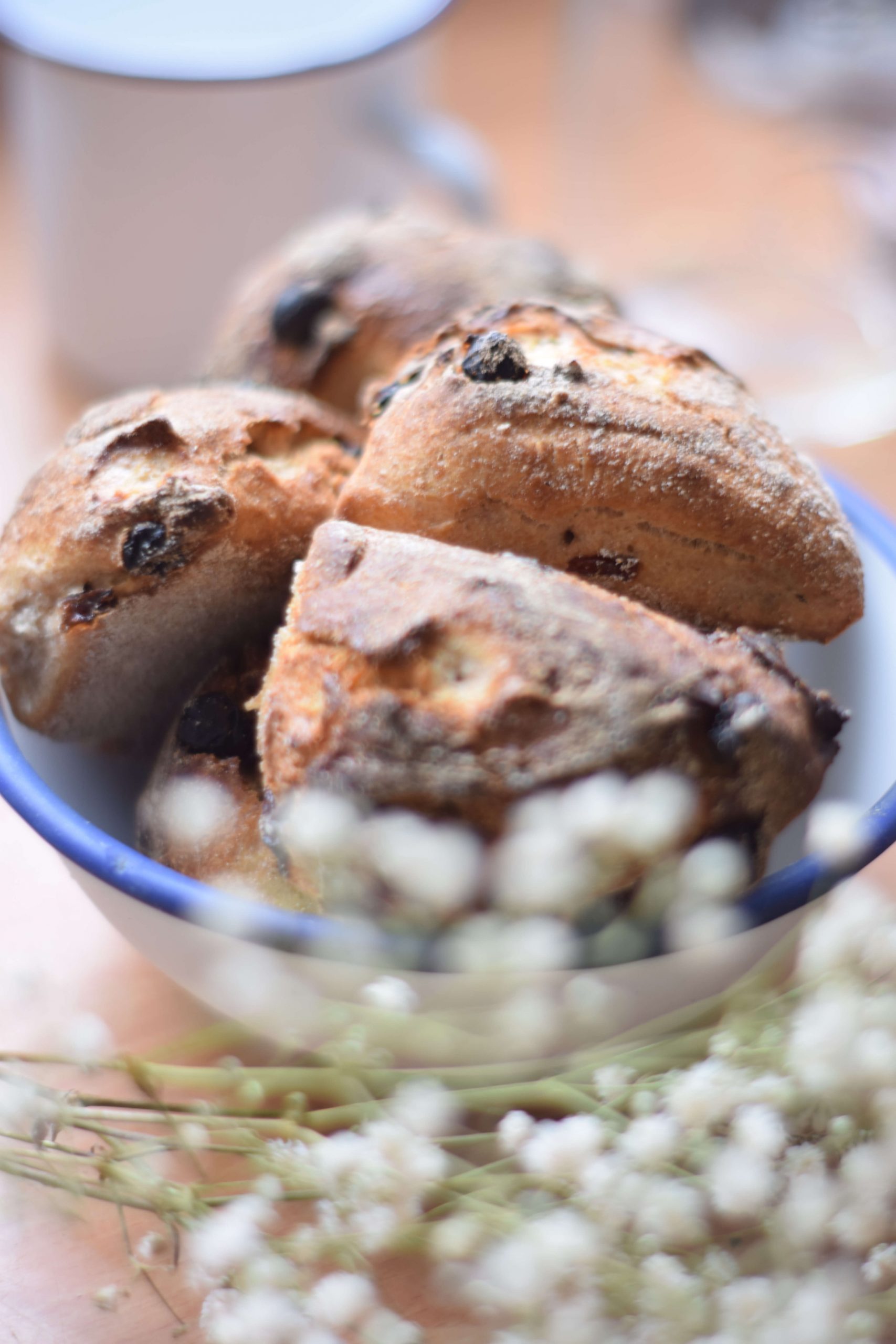 Enamel bowl with blue rim and freshly baked sourdough raisin buns with blurry gypsum herb in the front