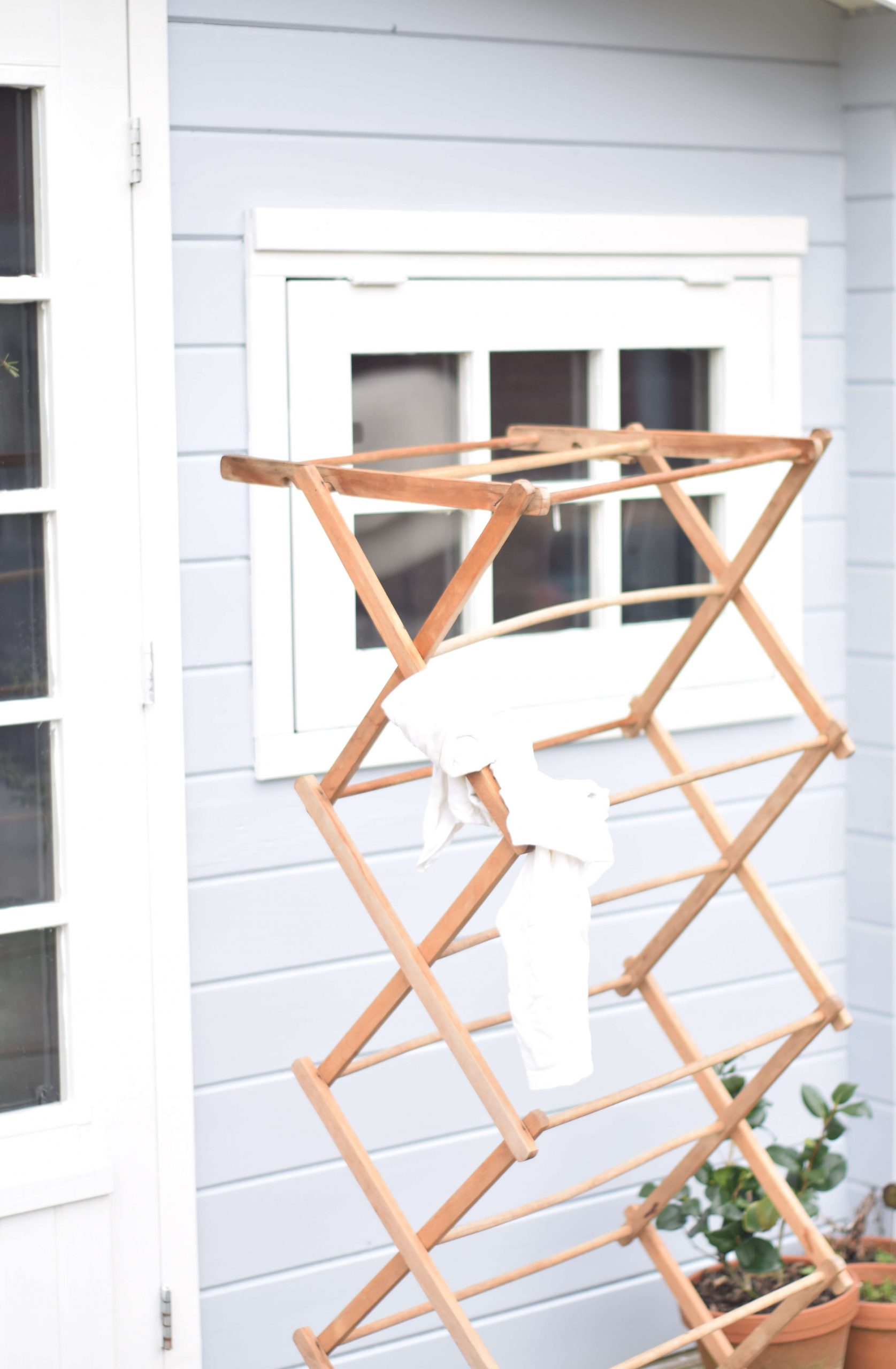 Wooden drying rack with a white towel in front of a light grey and white shed.