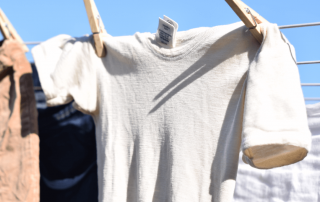 A warm white colored onesie is pegged on the washing line. Drying outside in the clear blue sky