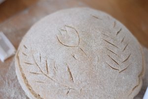 Freshly scored sourdough bread with a wheat scoring pattern and a tulip in the middle