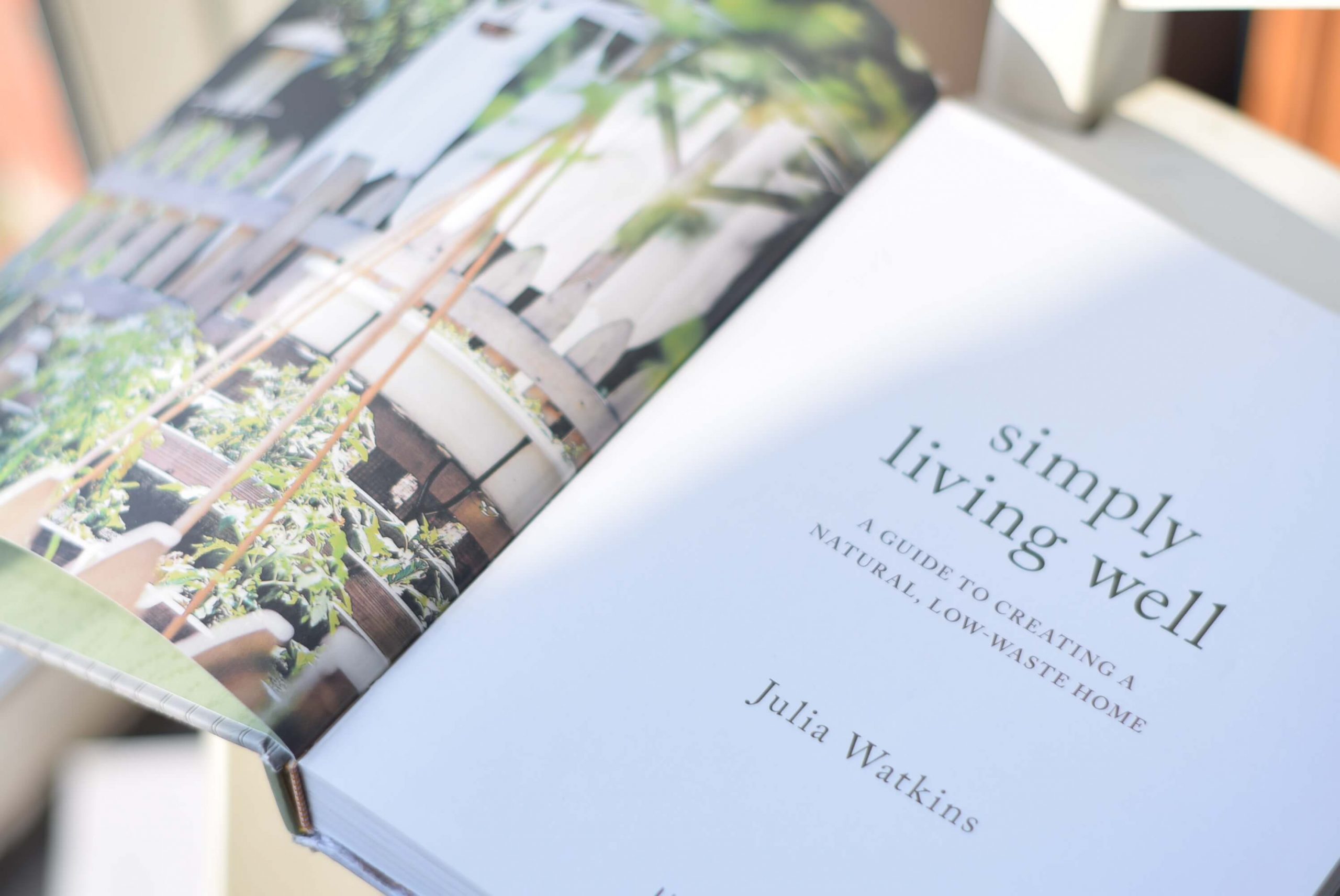 The book Simply Living Well by Julia Watkins opened to one of it's first pages. The left page has a picture of a garden and on the right is written text.