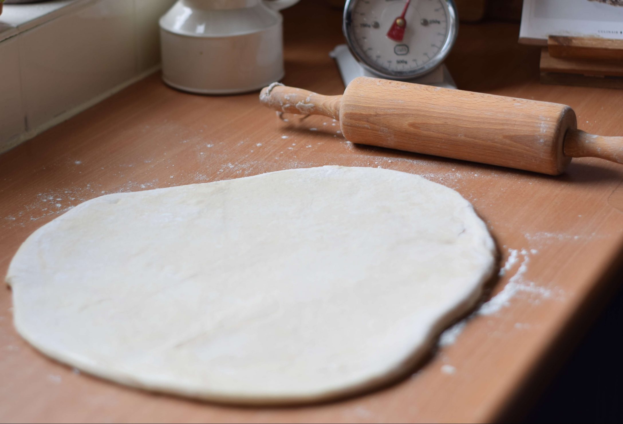 Kitchen counter with a round piece of rolled out sourdough doughnut dough. A wooden rolling pin it lying beside.