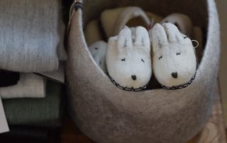 Upcycling idea using wool felt: A pair of wool felted bunny slippers in a light brown wool felted basket.