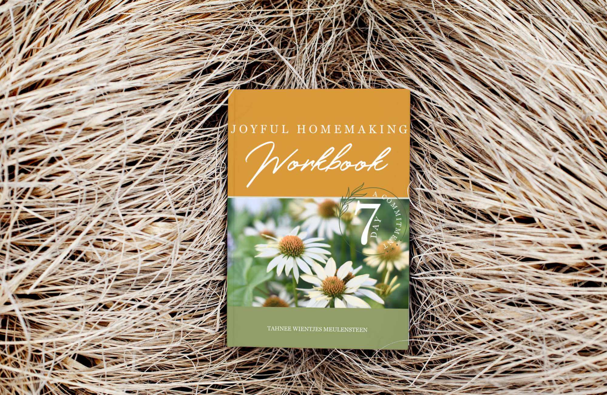 Joyful Homemaking' paperback book lying on a bed of straw, symbolizing the joy and warmth of homemaking in a natural and rustic setting.