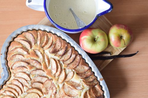 Freshly baked apple pie with slices of apple on top. Vanilla sauce and apples lying beside the pie.