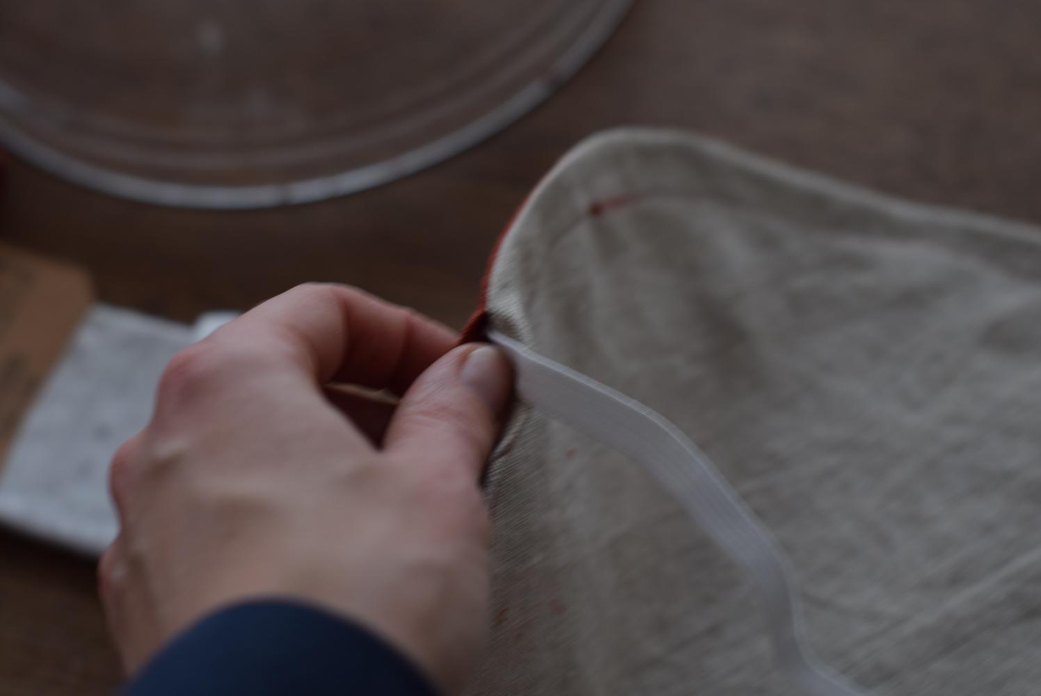 In this image, a safety pin is used to guide elastic through the fabric tunnel, ensuring a secure and adjustable fit for the fabric bowl cover. This