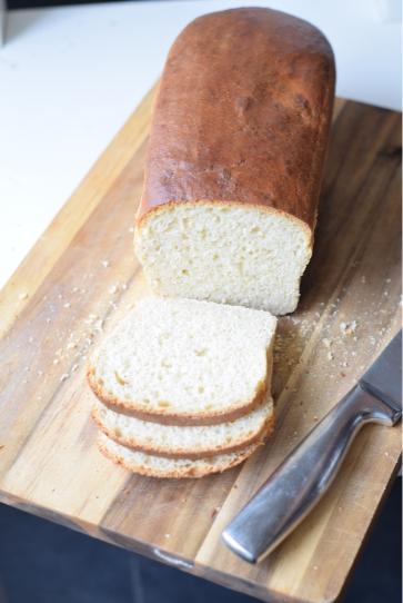 A loaf of multigrain sandwich bread sliced and placed on a wooden board.