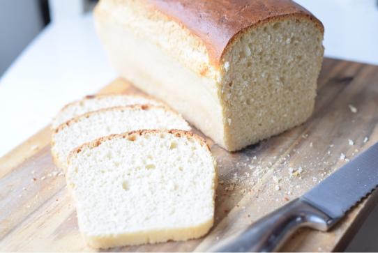 A close-up of a slice of light and fluffy sandwich bread on a wooden cutting board.