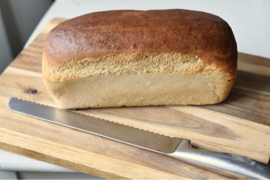 A loaf of freshly baked multigrain sandwich bread on a wooden cutting board.