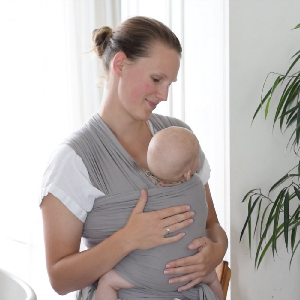 A mother carries her baby in a cozy grey wrap, symbolizing love and nurturing in their special moment together.