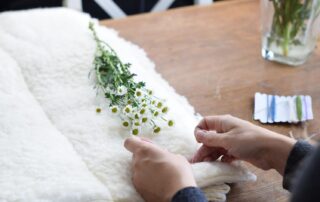 Chamomile flowers on a wool blanket. A homemaker is sewing a mattress.