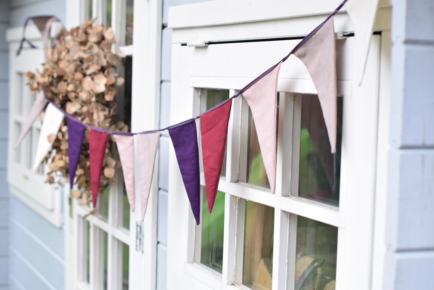 A bunting for special occasions made with rose colored linen fabric hanging outdoors in front of a window.