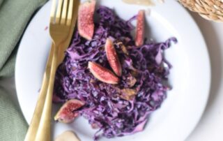 Warm and spicy red cabbage salad with raisins, sesame seeds, and a garam masala tahini dressing, garnished with fresh lemon slices and sesame seeds in a white serving bowl.