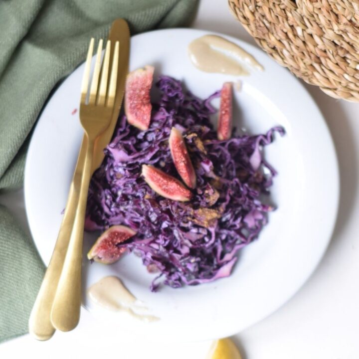 Warm and spicy red cabbage salad with raisins, sesame seeds, and a garam masala tahini dressing, garnished with fresh lemon slices and sesame seeds in a white serving bowl.