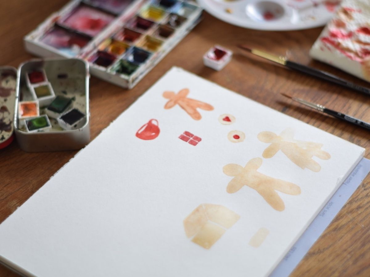 Watercolor supplies and a piece of watercolor paper with gingerbread men painted on them.