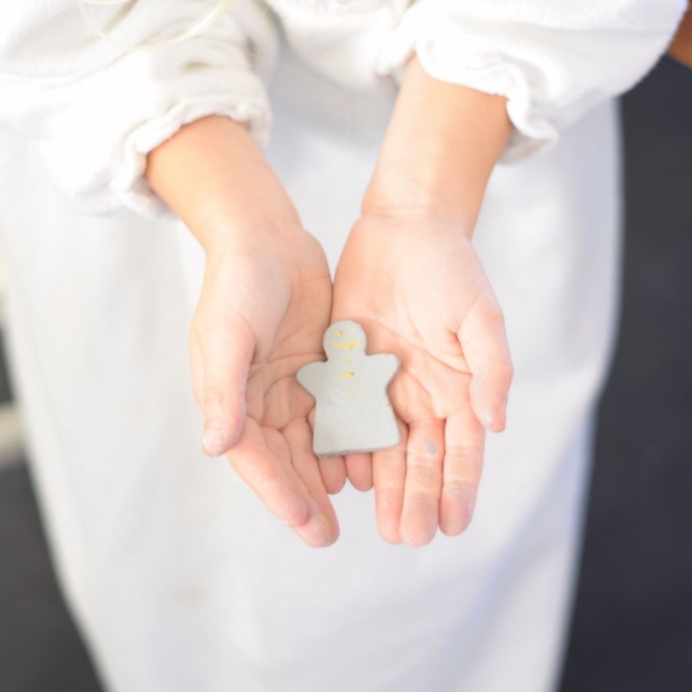 Two hands gently holding a handmade clay gingerbread man ornament, a thoughtful and creative Christmas gift.