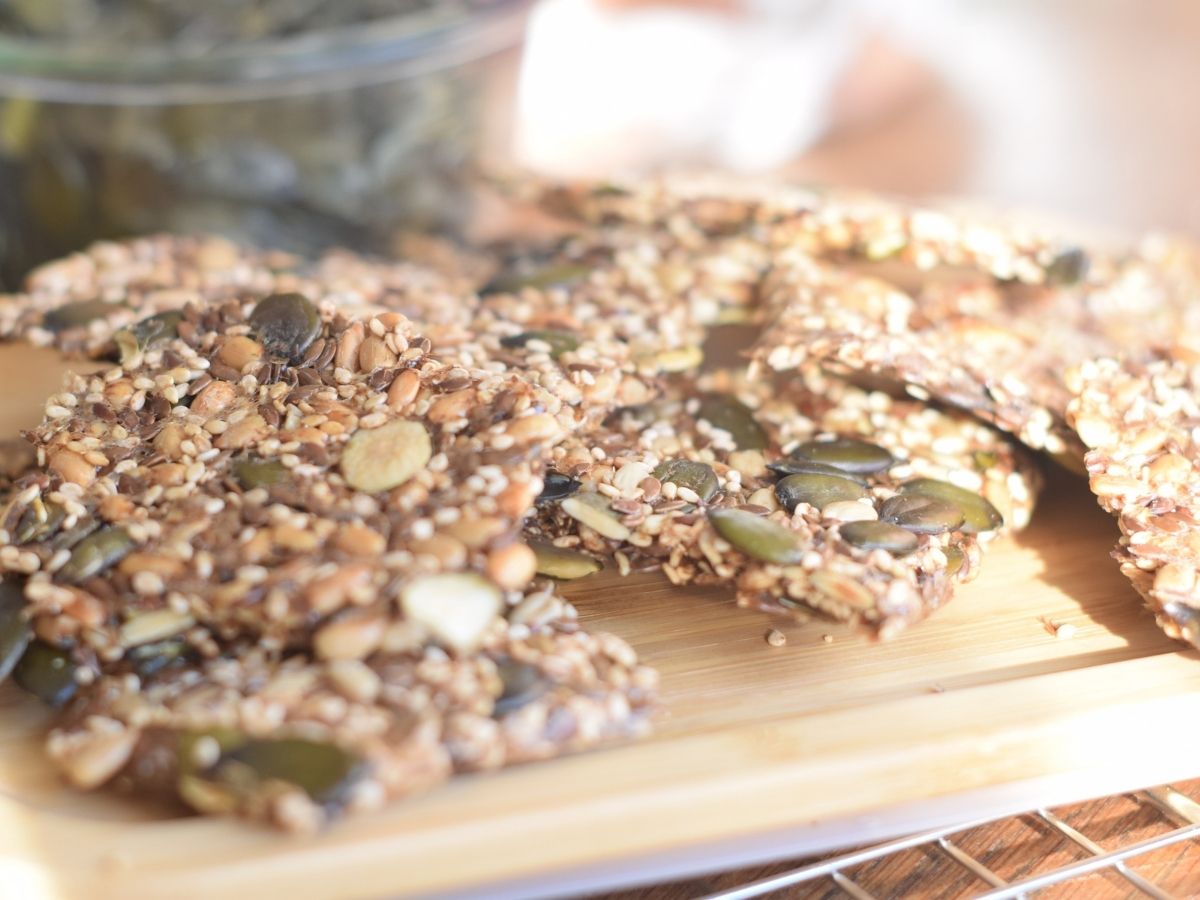 Close-up of crispy seed crackers resting on a cooling rack, with jars of seeds blurred in the background.