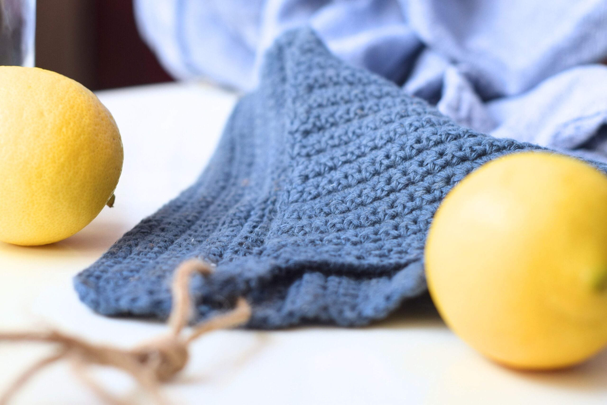 Close-up of a crocheted blue linen dishcloth lying on a flat surface with lemons.