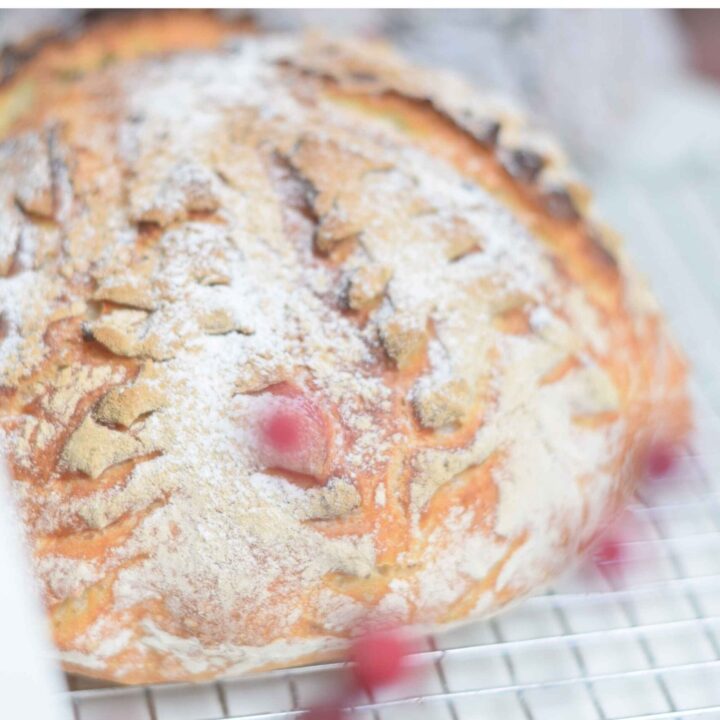 Scored bread with a spruce scoring pattern. Red berries in the front.