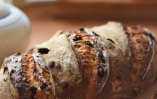 A freshly baked easy sourdough raisin bread on a cutting board, accompanied by a lovely teapot, perfect for tea time.