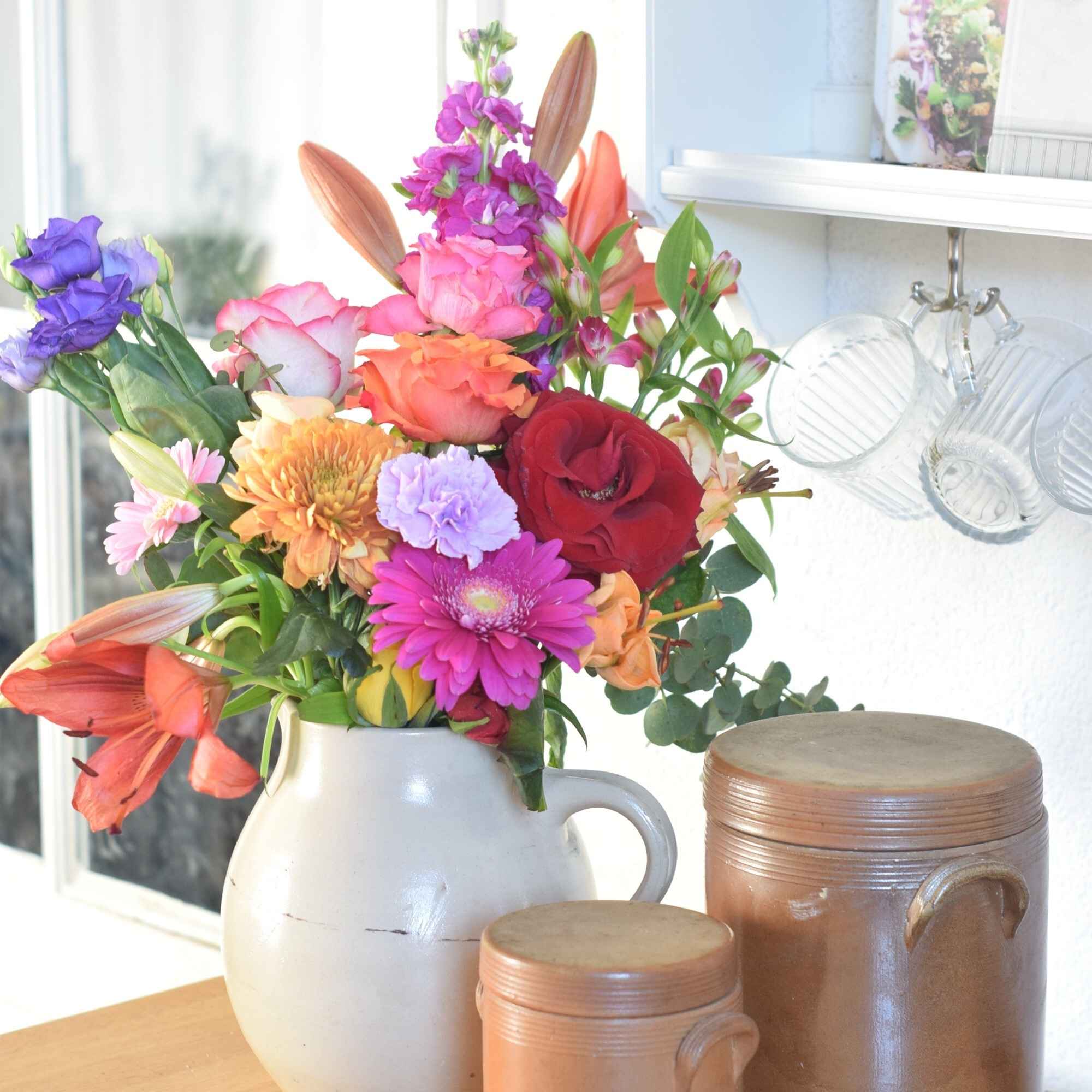 Colorful bouquet in a cream colored vase with light brown vintage pots.